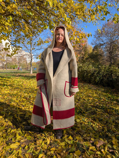 Woman with a loose hooded wool blanket coat in oatmeal and red. The model can be worn belted or loose.