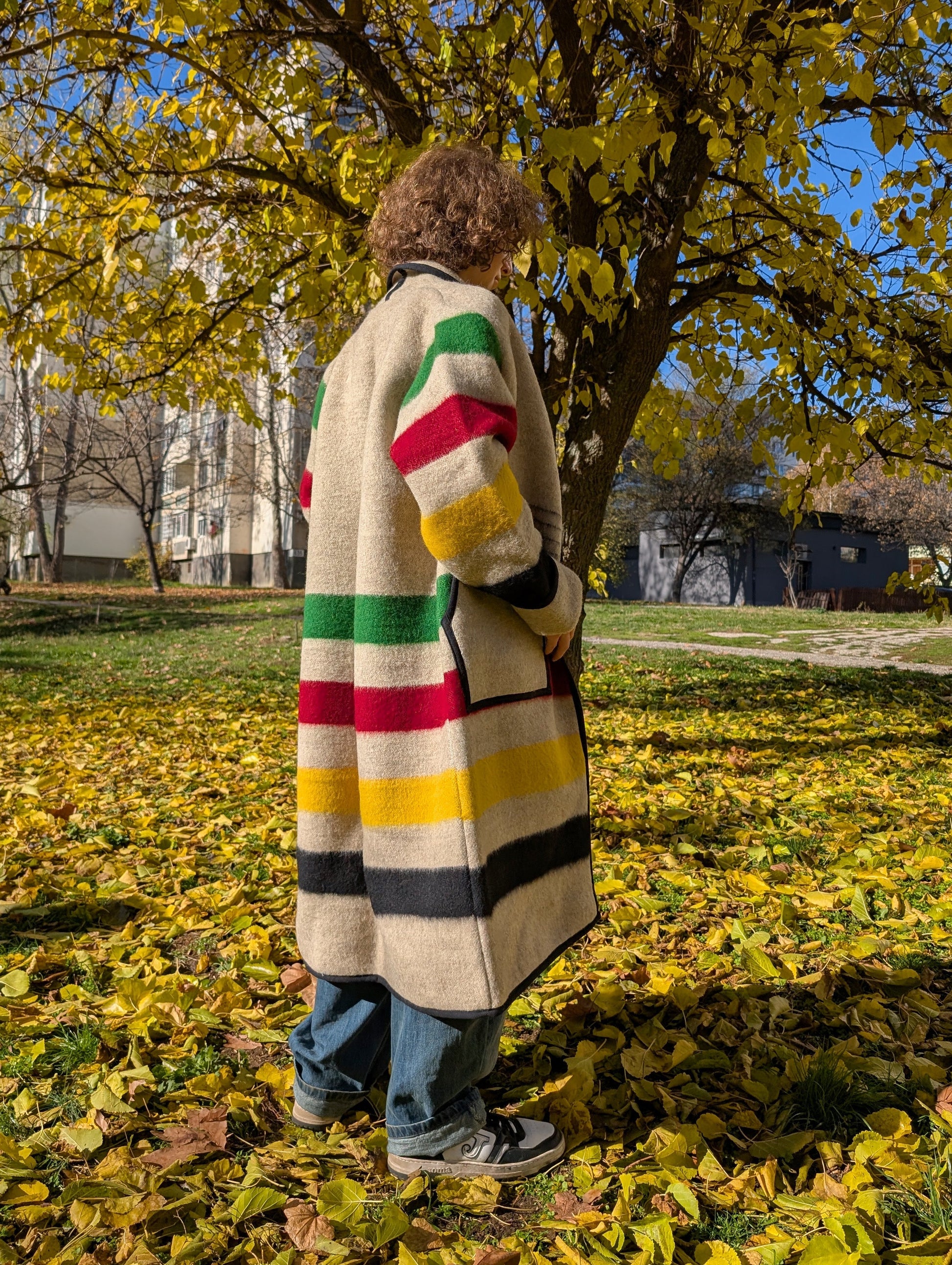 A young man wearing a long gray multi stripe blanket cardigan coat.