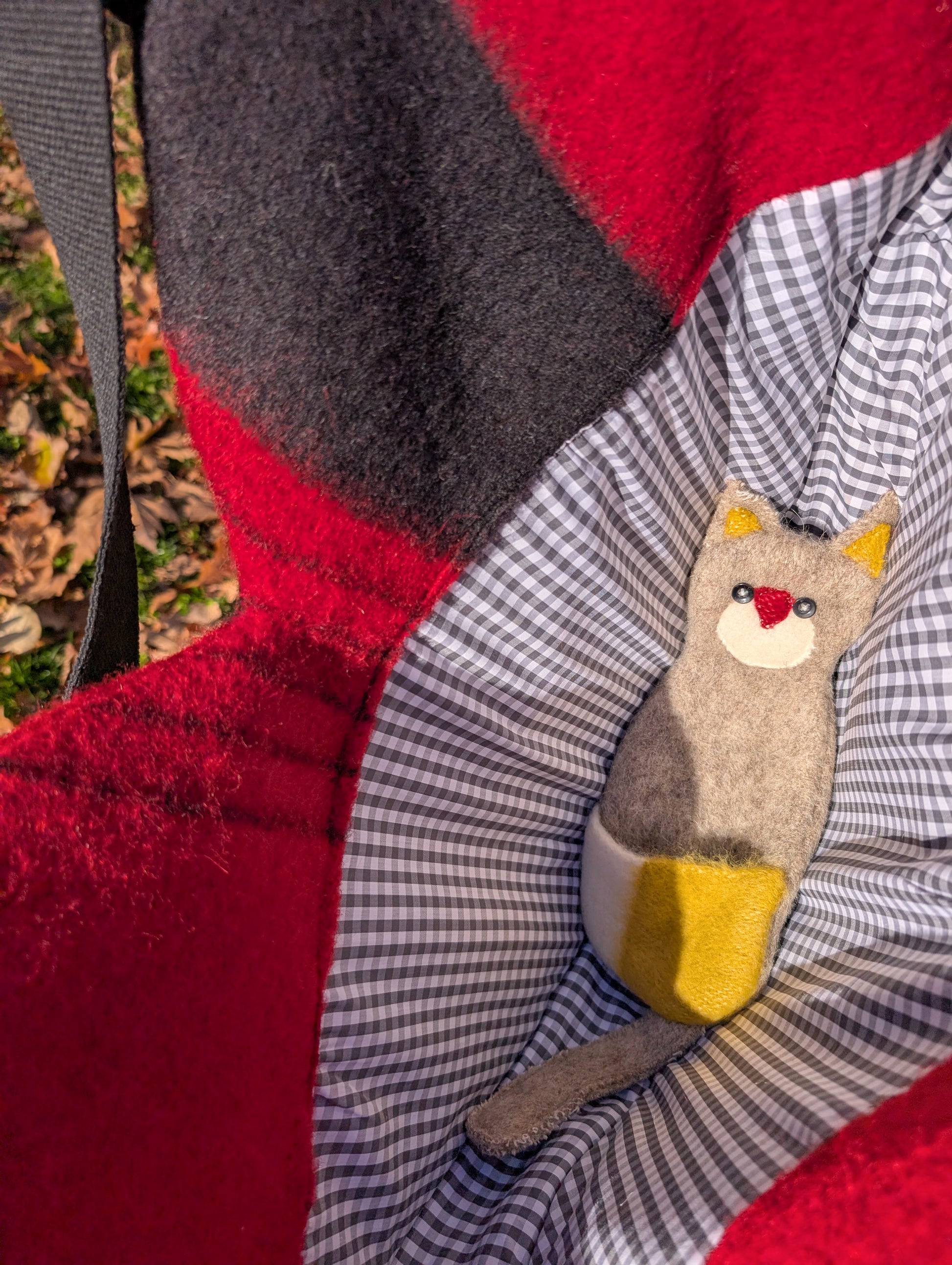 The inside of a red heart shaped tote bag with a cute checkered cotton lining and a plush toy cat in.