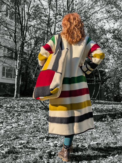 Woman wearing a duster coat and a matching large shoulder bag, both made from virgin wool blanket. Bold traditional colorful stripes make a modern statement style. 