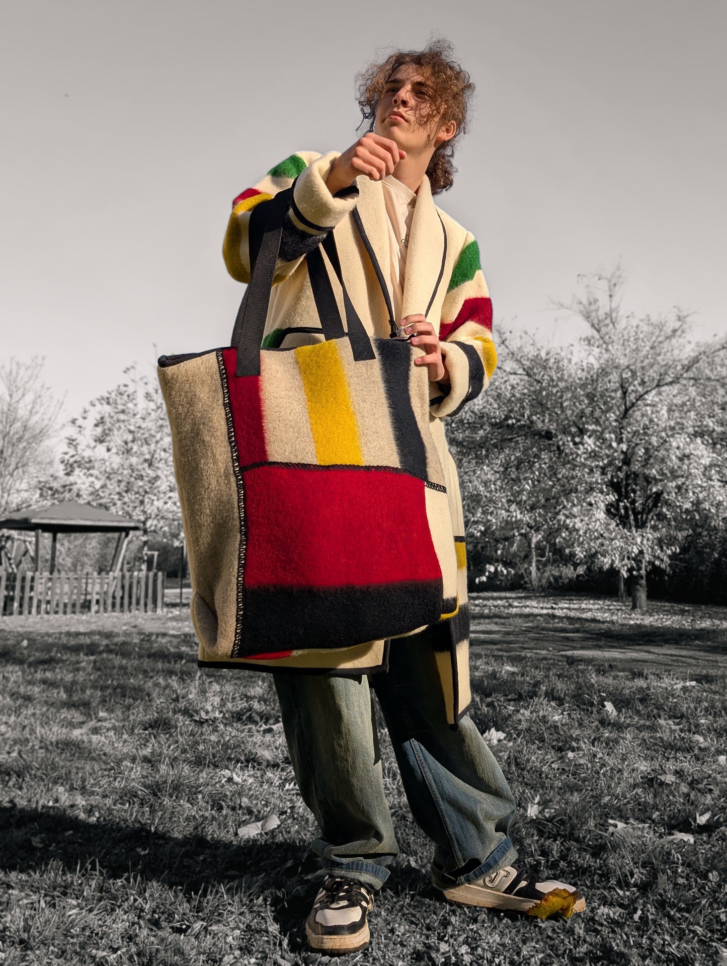 Young man wearing a modern shoulder bag made from wool blanket patches in bold colors - red, yallow, black - on earth gray base. The bag is comfy, stylish and functional.
