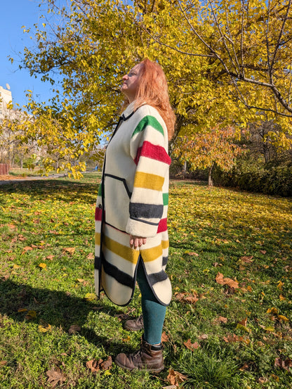 A woman posing at one side with a duster coat featuring side slits, classic collar and button closure. The multi stripes honor the times.