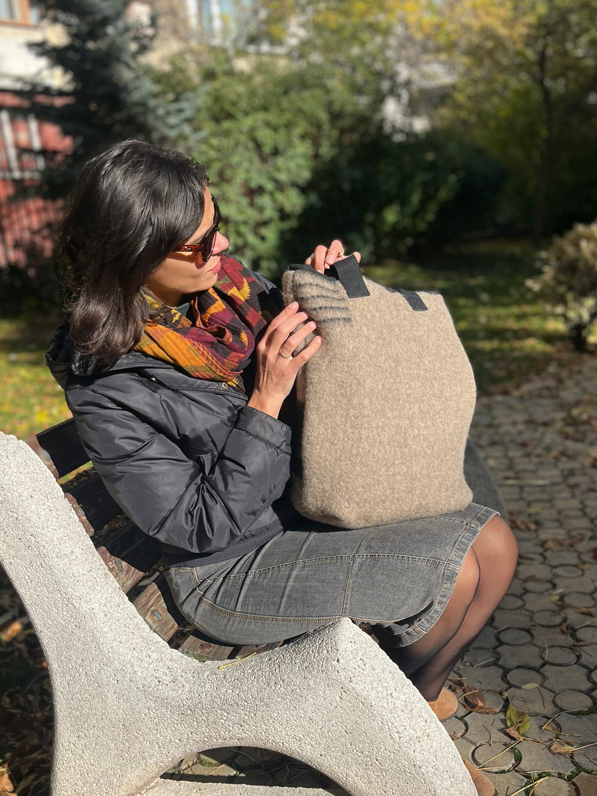 Woman sitting on a bench holding a a soft gray bucket bag in an outdoor setting.