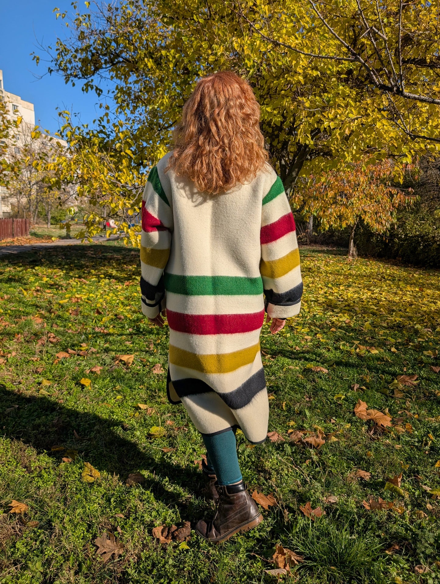 A woman posing with an evergreen blanket duster coat with side slits, classic collar and button closure. Handwoven wool crafted outerwear, slow fashion.