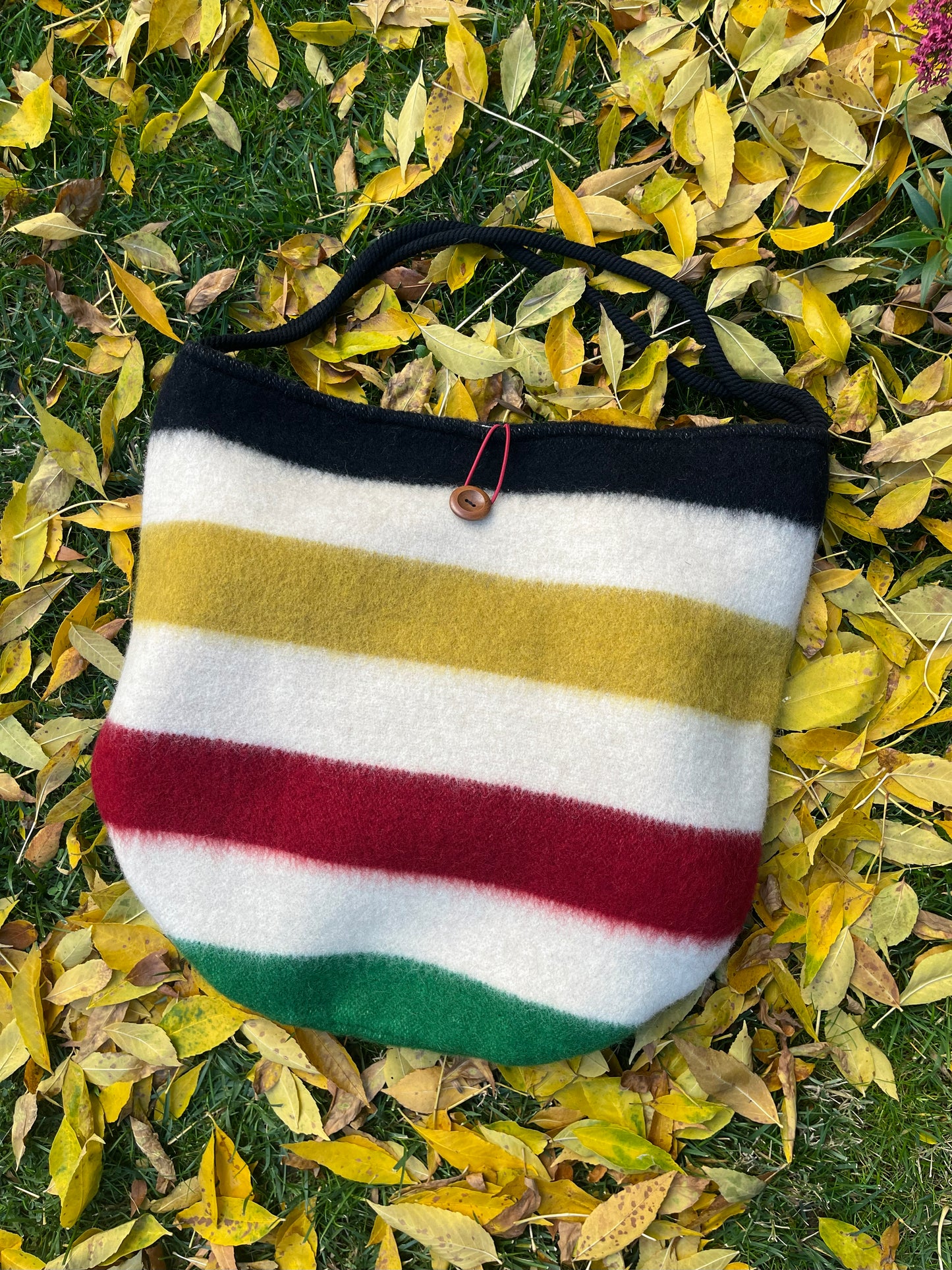Modern stylish boho slow fashion bag made from luxurious blanket cuts laying on a bed of autumn leaves.