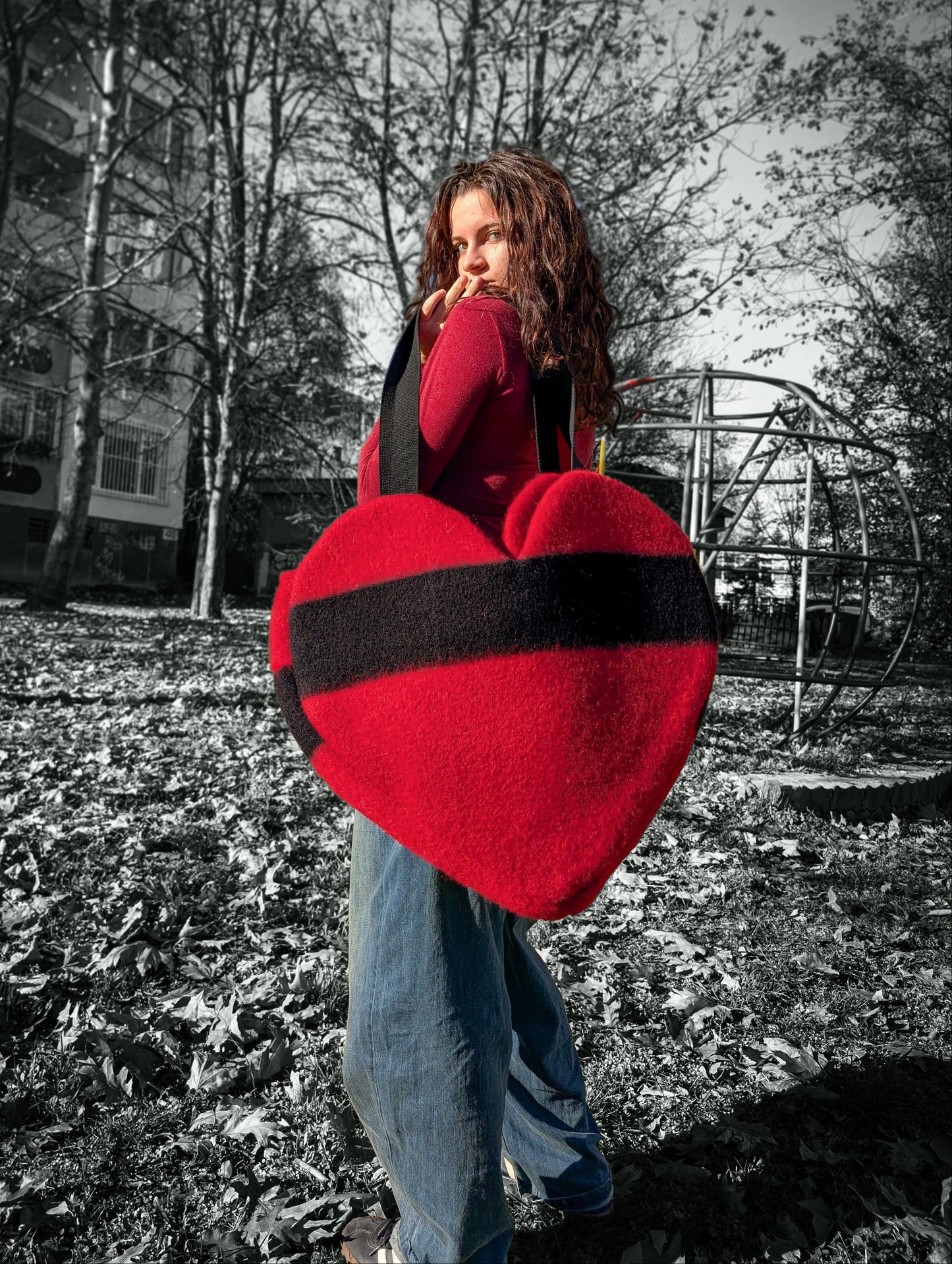 Young woman holding a large red heart-shaped object outdoors on a sunny day.
