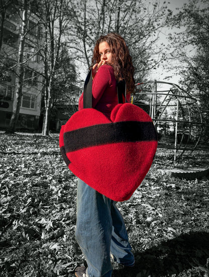 Young woman holding a large red heart-shaped object outdoors on a sunny day.