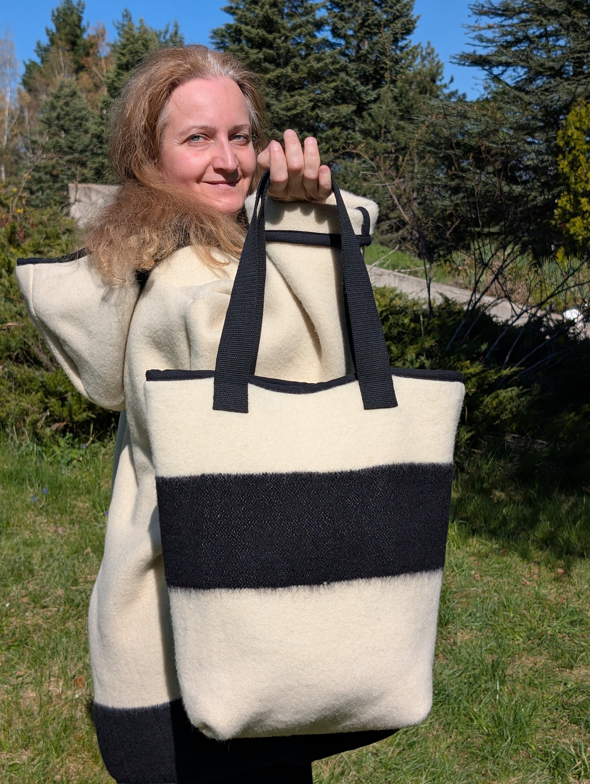 Woman holding a large off-white woolen tote bag with a single wide black stripe