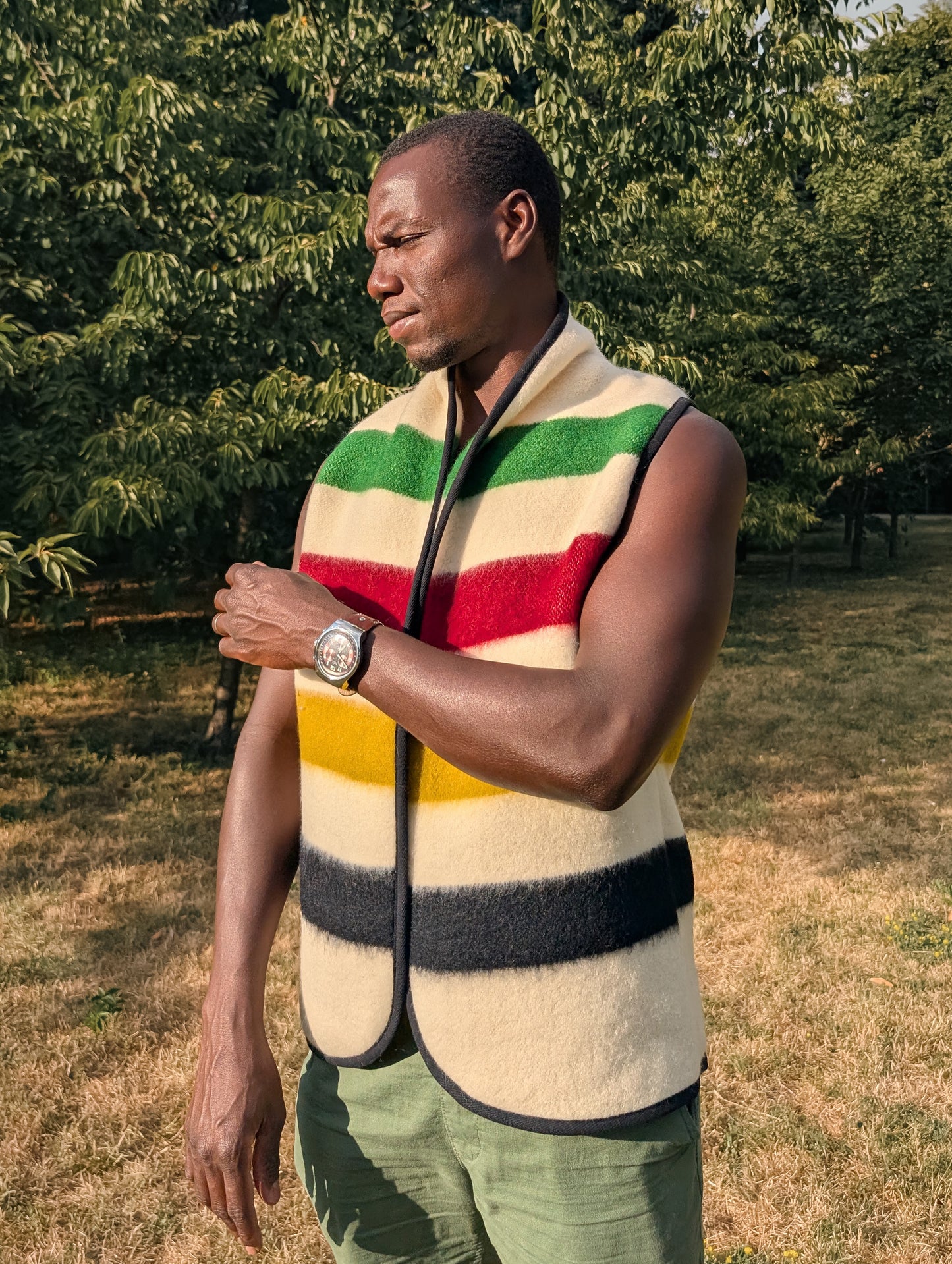 Man wearing a colorful striped vest or sleeveless jacket outdoors with trees in the background