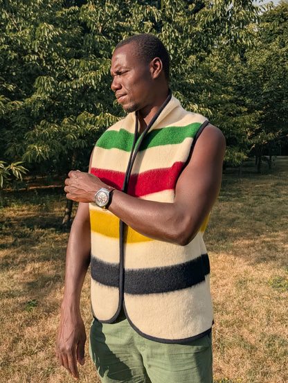 Man wearing a colorful striped vest or sleeveless jacket outdoors with trees in the background