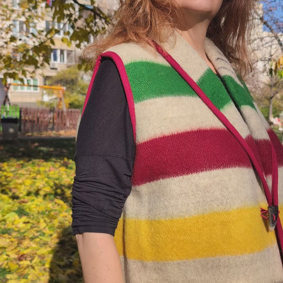 Video of a woman wearing a stylish blanket vest in earth gray base with statement colorful stripes, robe collar and a horn button. 