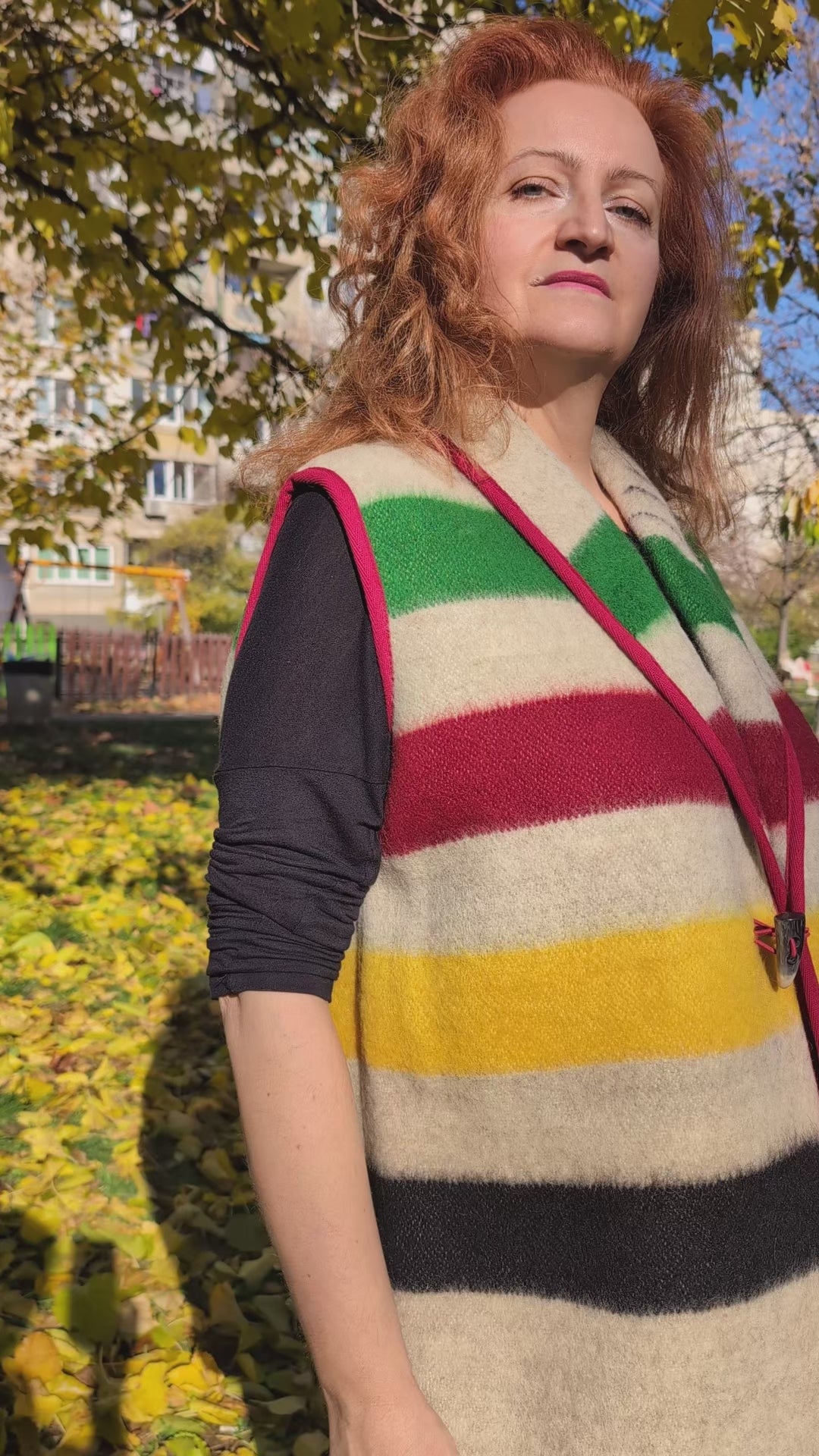 Video of a woman wearing a stylish blanket vest in earth gray base with statement colorful stripes, robe collar and a horn button. 