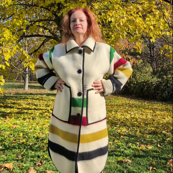 A woman wearing a blanket duster coat with with single breasted button closure, side slits and two front pockets. Unisex model, thick pure wool outerwear.
