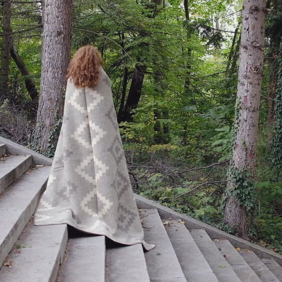 Video of woman unwrapping and draping an eco-luxury wool blanket with earth tones and ancient geometric design pattern. Ideal for modern and rustic home decors.