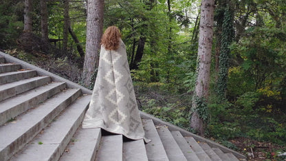 Video of woman unwrapping and draping an eco-luxury wool blanket with earth tones and ancient geometric design pattern. Ideal for modern and rustic home decors.