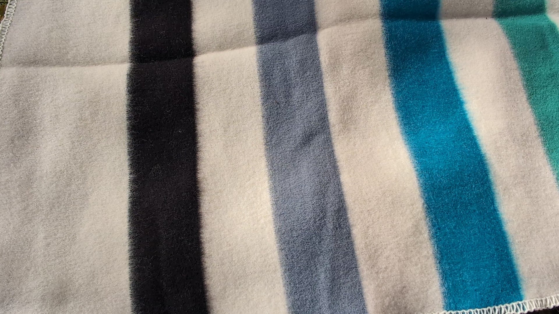 video of handspun virgin wool blanket with stripes in blue gray and green tones.