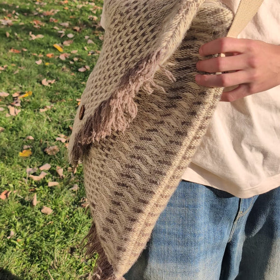 Person showcasing a wool blanket messenger bag with structured pattern and soft natural tones.