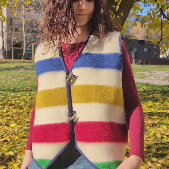 A young woman wearing a beautiful upcycled blanket sleeveless gilet with designer's stripes, tailer as a unisex vest, suitable for reenactment, everyday- and street wear.