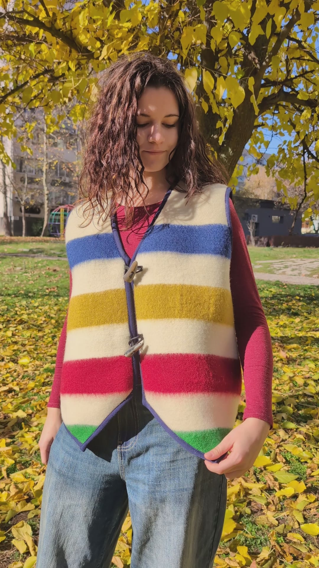 A young woman wearing a beautiful upcycled blanket sleeveless gilet with designer's stripes, tailer as a unisex vest, suitable for reenactment, everyday- and street wear.