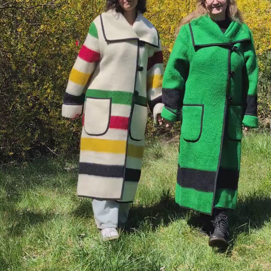 A video showing two women wearing same model long collar coats, one in solid traditional green with black stripe, and the other in ivory with multicolor stripes. Upcycled wool blanket dustercoats.