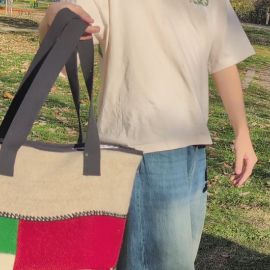 A video of a young man demonstrating a large fashionable upcycled patcwork tote bag with colorful panels in bold traditional colors on gray base. 