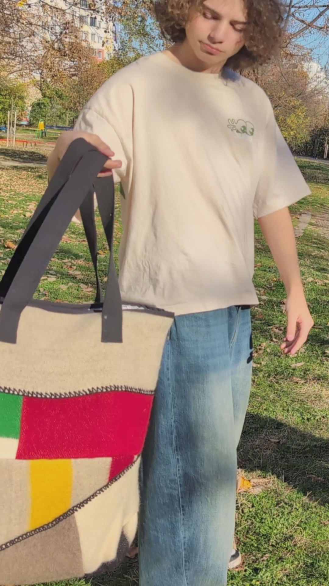 A video of a young man demonstrating a large fashionable upcycled patcwork tote bag with colorful panels in bold traditional colors on gray base. 